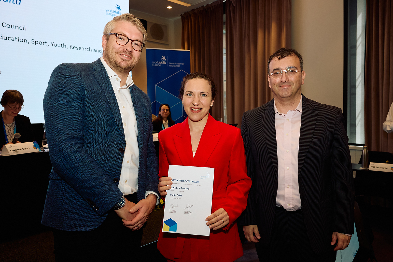 Three people pose together, with the person in the centre holding a WorldSkills Europe membership certificate for Malta.