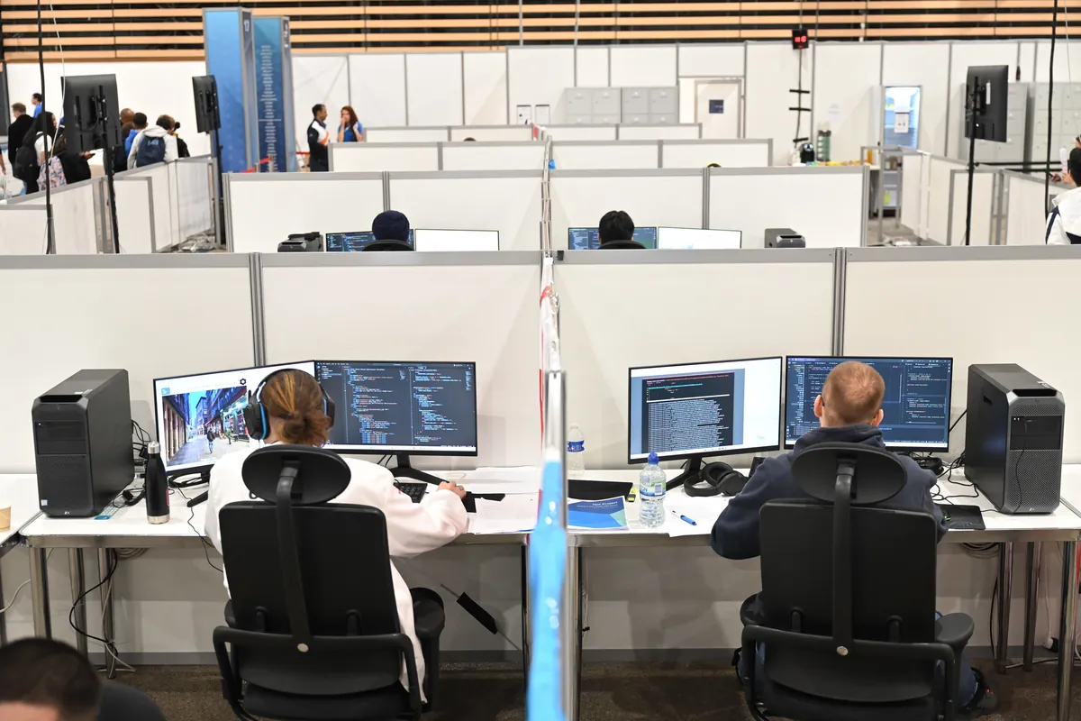 Participants work at computers displaying code in individual partitioned workstations at a skills competition.